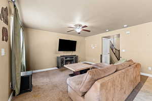 Carpeted living area with ceiling fan and a lit fireplace