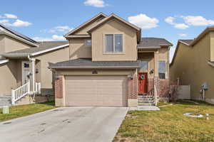 Traditional-style home with brick siding, a garage, a front lawn, and stucco siding