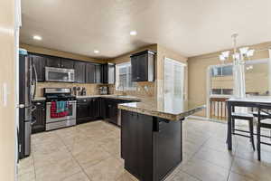Kitchen featuring a peninsula, stainless steel appliances, tasteful backsplash, a kitchen bar, and a chandelier
