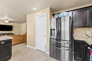 Kitchen featuring stainless steel refrigerator with ice dispenser, light stone countertops, light tile patterned floors, a ceiling fan, and recessed lighting