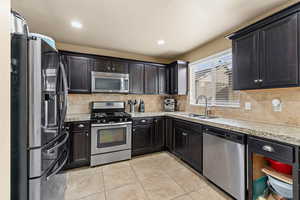 Kitchen featuring stainless steel appliances, decorative backsplash, light stone countertops, light tile patterned floors, and recessed lighting