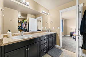 Full bathroom with double vanity, light colored carpet, a walk in closet, light tile patterned floors, and connected bathroom