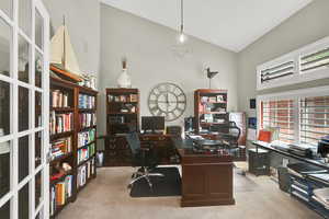 Home office with vaulted ceiling and light colored carpet