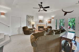Living area featuring a ceiling fan, a tile fireplace, french doors, and light colored carpet