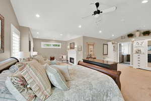 Bedroom with vaulted ceiling, a warm lit fireplace, light colored carpet, recessed lighting, and multiple windows