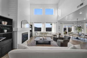 Living area with light wood-style flooring, a large fireplace, recessed lighting, and a high ceiling