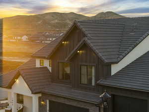 Property exterior at dusk with brick siding, a mountain view, board and batten siding, a tiled roof, and an attached garage