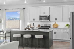 Kitchen featuring a kitchen island with sink, a kitchen breakfast bar, light stone countertops, light wood finished floors, and stainless steel appliances