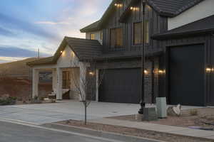 View of front of house with concrete driveway, a tiled roof, board and batten siding, and brick siding