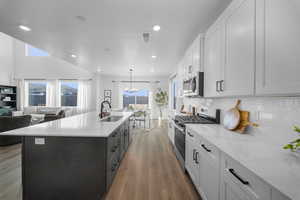 Two tone kitchen with two tone color scheme, stainless steel appliances, hanging lights, light stone counters, and dark wood-style flooring
