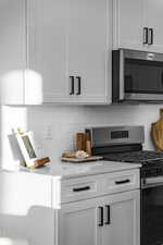 Kitchen featuring stainless steel appliances, white cabinets, light stone counters, and decorative backsplash