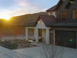 View of front of house with a tiled roof, a patio area, brick siding, concrete driveway, and an attached garage