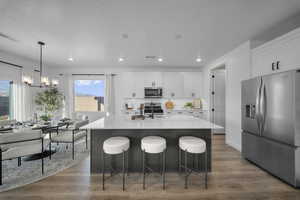 Two tone kitchen with stainless steel appliances, a kitchen breakfast bar, hanging lights, an island with sink, and light stone counters