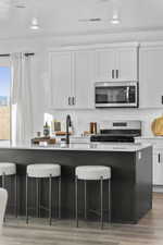 Kitchen featuring a breakfast bar, range with electric cooktop, stainless steel microwave, a kitchen island, and backsplash