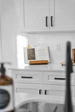 Kitchen view of white cabinetry, light stone counters, and decorative backsplash