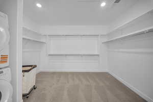 Walk in closet featuring light carpet and stacked washer and dryer