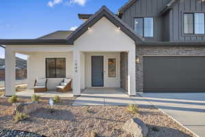 View of front facade featuring stone siding, board and batten siding, concrete driveway, covered porch, and an attached garage