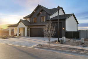 View of front facade featuring concrete driveway, a tiled roof, board and batten siding, and an attached garage