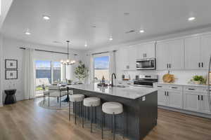 Kitchen featuring a chandelier, stainless steel appliances, a center island with sink, a breakfast bar area, and light stone countertops