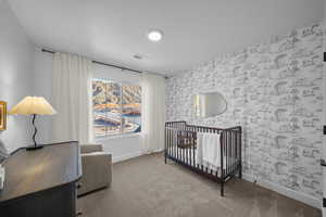 Bedroom featuring carpet, a crib, and wallpapered walls