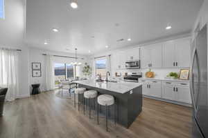 Kitchen featuring two tone cabinets, a breakfast bar, hanging lights, a center island with sink, and stainless steel appliances