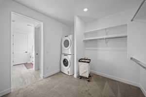 Laundry room featuring light colored carpet and stacked washer / drying machine