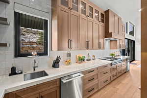 Kitchen featuring light stone counters, stainless steel appliances, glass fronted cabinets, light wood-style flooring, and tasteful backsplash