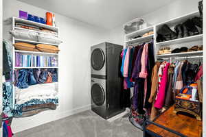 Laundry area featuring stacked washer / dryer and light colored carpet