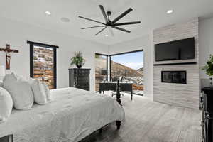 Primary bedroom with multiple windows, ceiling fan, a fireplace, light colored carpet, and recessed lighting