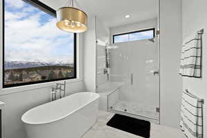 Primary bath with a shower stall, a freestanding bath, light marble finish floors, recessed lighting, and a mountain view