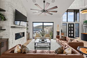 Living room with light wood-style floors, a high ceiling, a fireplace, and ceiling fan