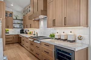 Kitchen with vaulted ceiling, open shelves, wine cooler, decorative backsplash, and light wood-type flooring