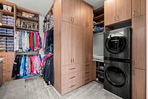 Primary closet area featuring stacked washer / drying machine, light carpet, and cabinet space