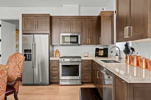 Kitchen with stainless steel appliances, light stone countertops, dark wood finish cabinets, and light wood-style floors