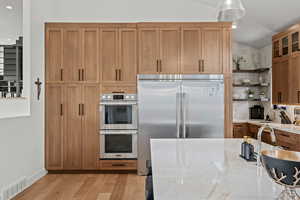 Kitchen featuring open shelves, stainless steel appliances, light stone countertops, light wood-type flooring, and lofted ceiling