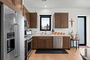 Kitchen featuring premium appliances, light wood-style flooring, recessed lighting, light stone countertops, and dark wood finish cabinets
