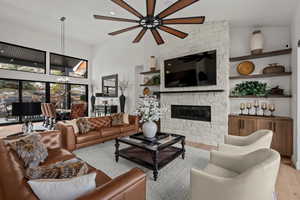 Living room with wood finished floors, a fireplace, a high ceiling, a chandelier, and ceiling fan