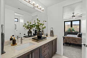 Ensuite bathroom featuring double vanity, light colored carpet, and ceiling fan