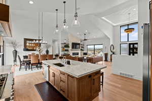 Kitchen featuring light stone countertops, light wood-type flooring, an island with sink, open floor plan, and lofted ceiling
