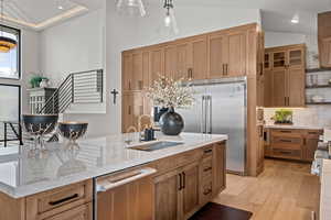 Kitchen featuring light stone countertops, high quality appliances, tasteful backsplash, light wood-style floors, and pendant lighting