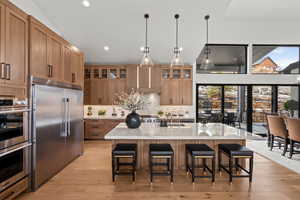 Kitchen featuring light stone counters, stainless steel appliances, a breakfast bar, decorative light fixtures, and a large island with sink