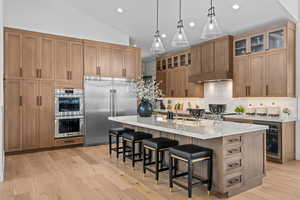 Kitchen with stainless steel appliances, a kitchen breakfast bar, a large island with sink, beverage cooler, and vaulted ceiling