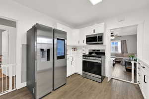 Kitchen featuring stainless steel appliances, white cabinetry, ceiling fan, light wood finished floors, and open floor plan