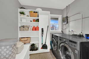 Laundry room with washing machine and dryer, electric panel, and light wood-style flooring