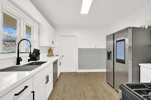 Kitchen with stainless steel appliances, white cabinetry, light wood finished floors, and decorative backsplash