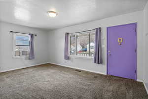 Carpeted spare room featuring a textured ceiling, plenty of natural light, and cooling unit