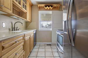 Kitchen featuring stainless steel appliances, glass fronted cabinets, light tile patterned floors, and wood finish cabinetry