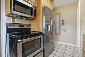 Kitchen featuring stainless steel appliances, light tile patterned flooring, light countertops, and light wood finish cabinets