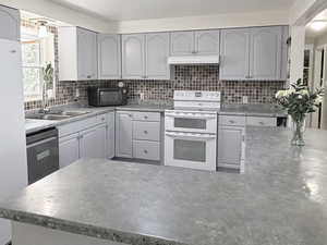 Kitchen featuring white appliances, backsplash, gray cabinetry, light countertops, and finished concrete floors