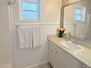 Full bath featuring a wainscoted wall, vanity, plenty of natural light, and light tile patterned floors